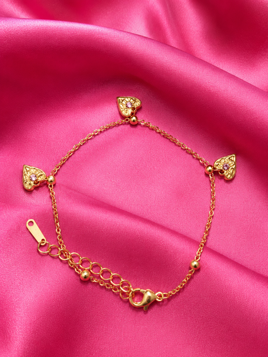 Gold bracelet with heart-shaped charms on a pink satin background