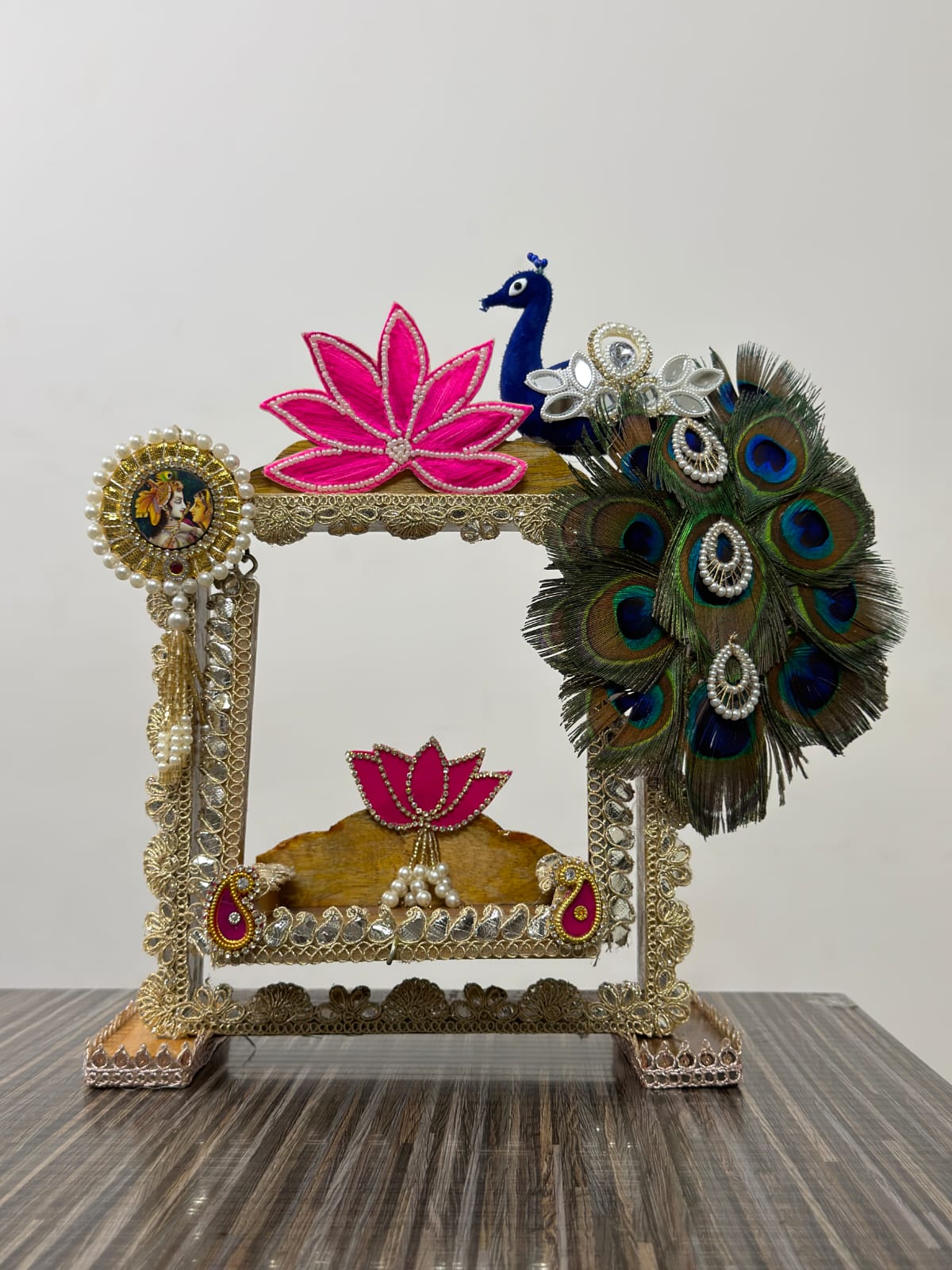 Handmade Krishna Jhula with real peacock feathers, gold filigree frame, pink lotus flowers, blue peacock figurine and Radha-Krishna medallion