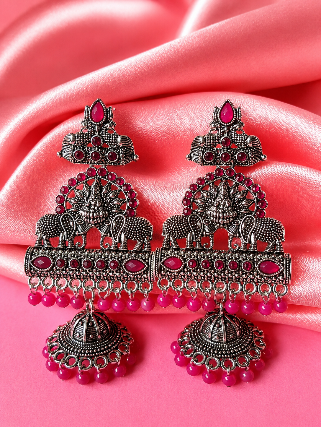 Ornate earrings with pink beads on a pink fabric background