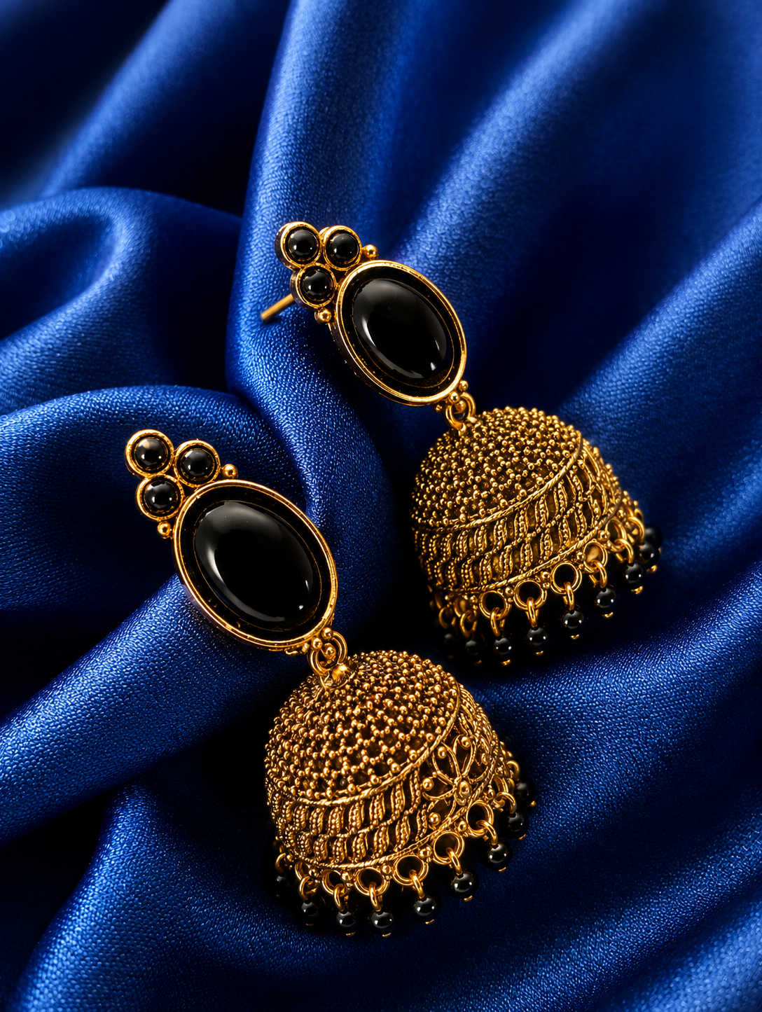 Gold and black earrings on a blue satin background