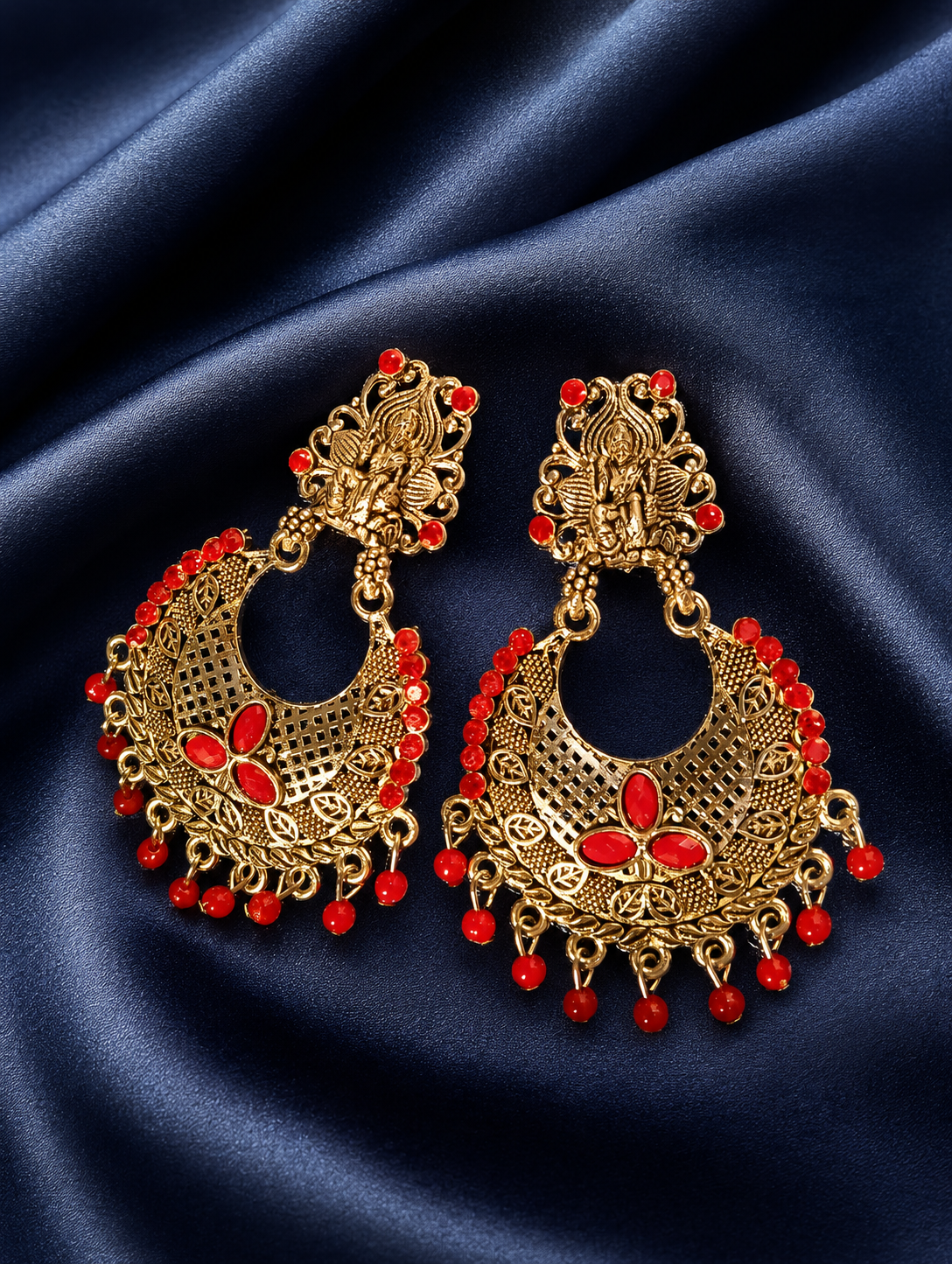 Gold and red earrings on a blue satin background