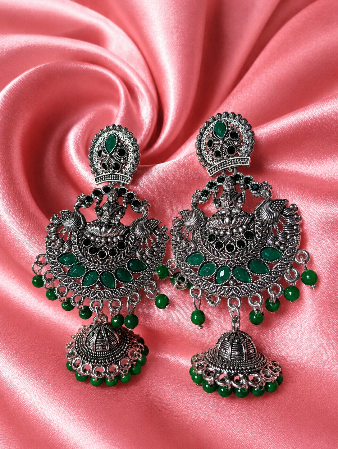 Ornate silver and green earrings on a pink satin background