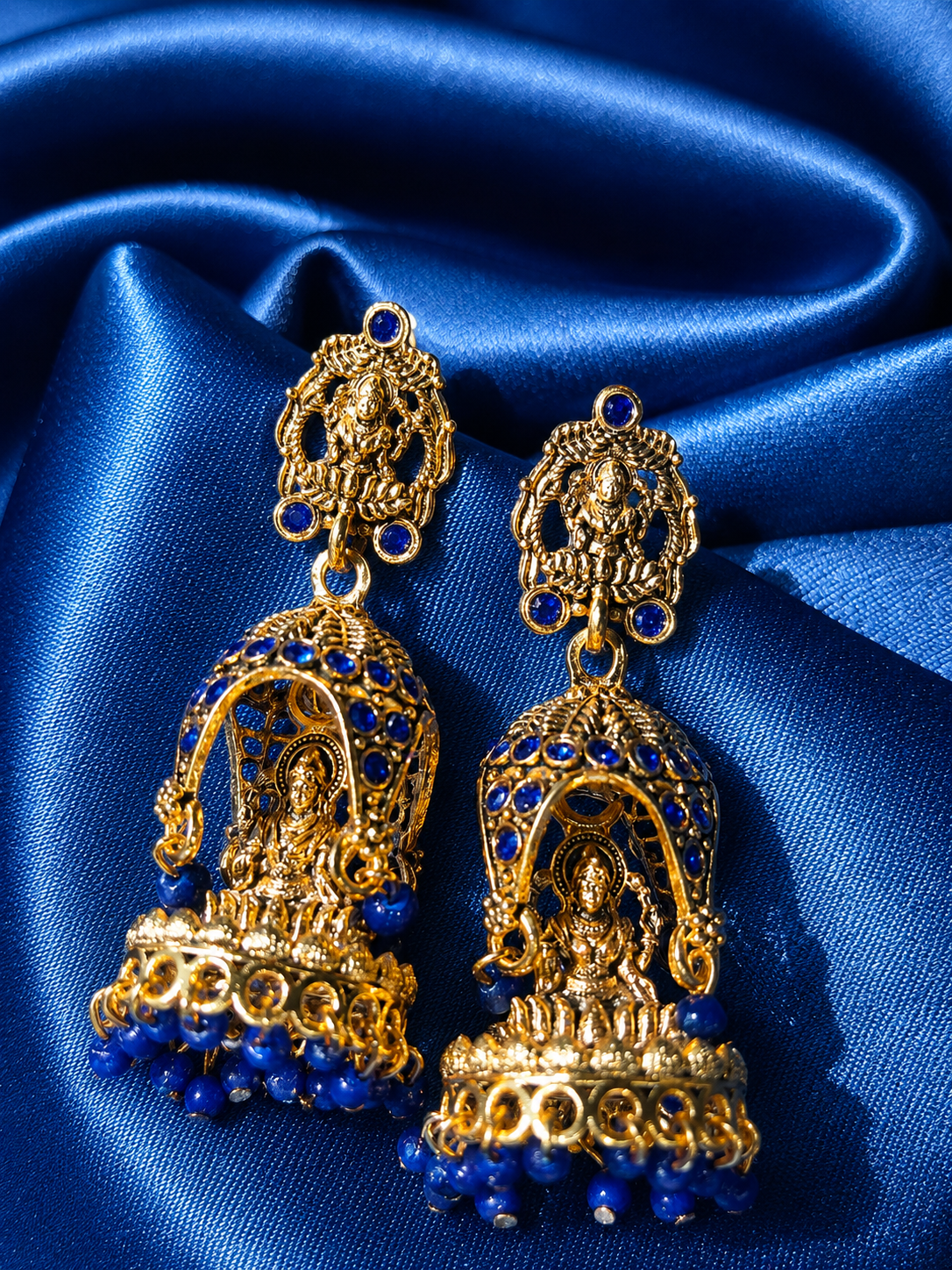 Gold and blue earrings on a blue satin background