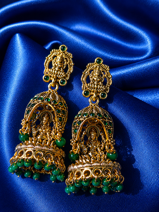 Gold and green earrings on a blue satin background