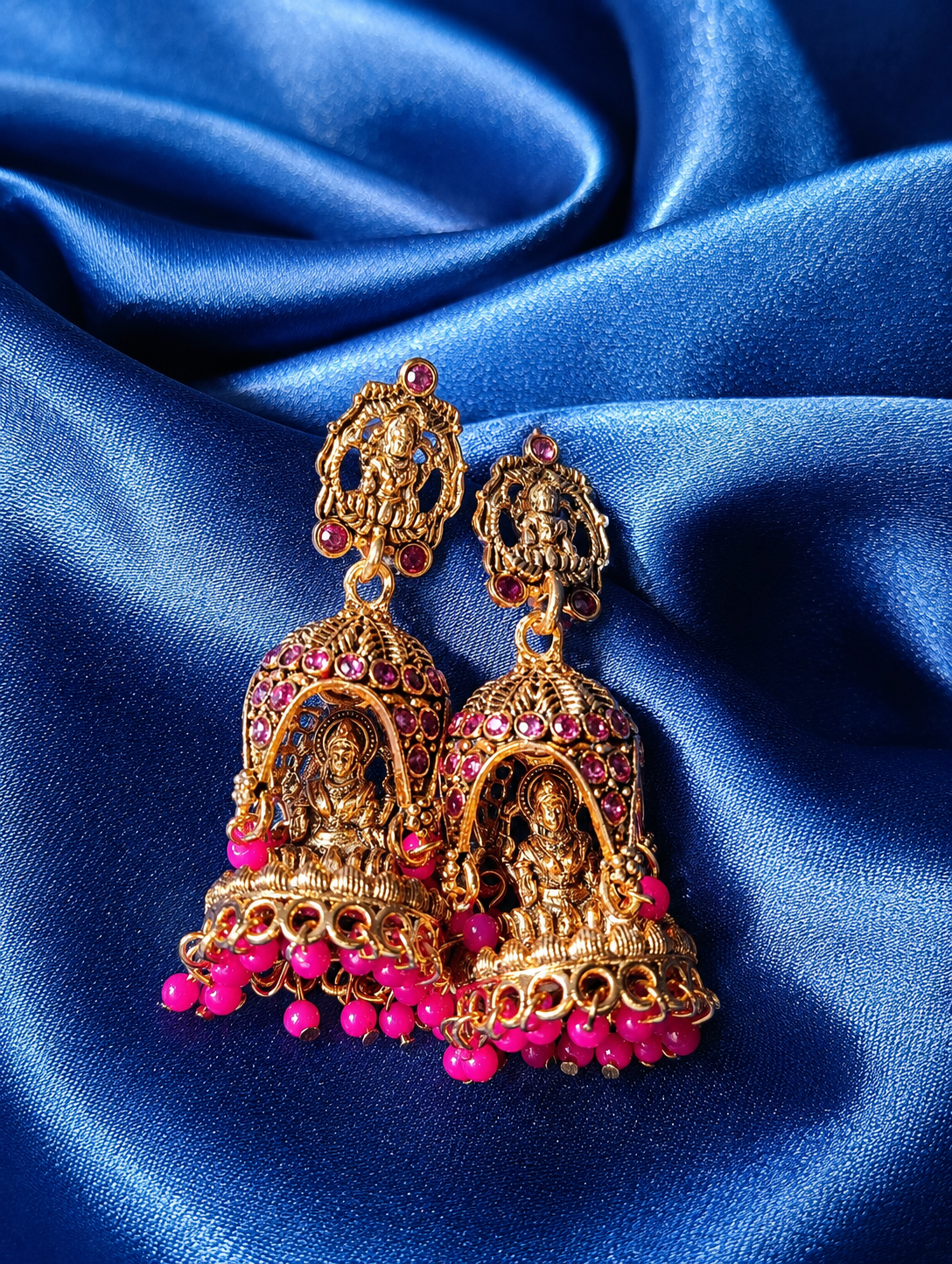 Gold and pink earrings on a blue satin background