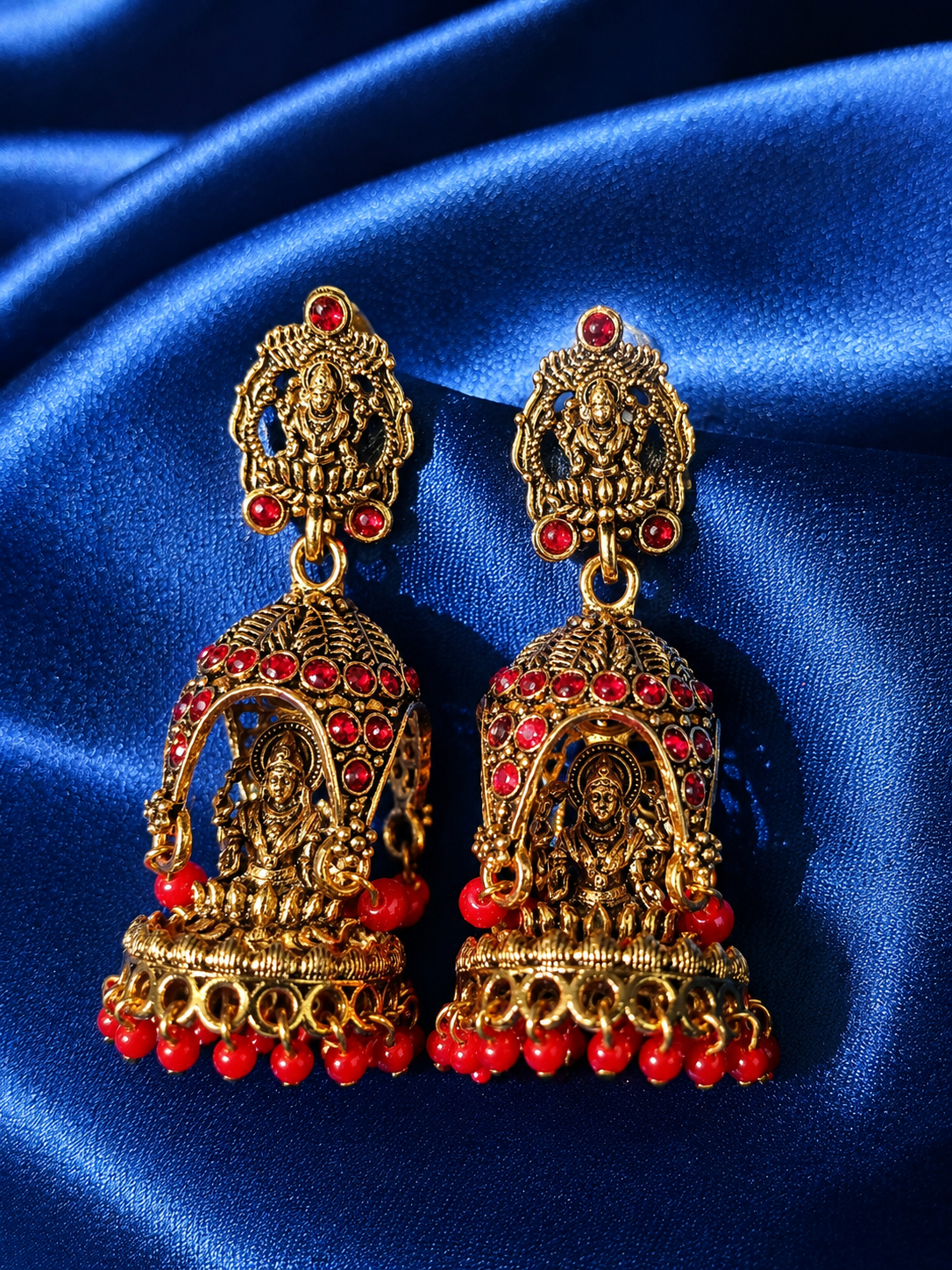 Gold and red earrings on a blue satin background