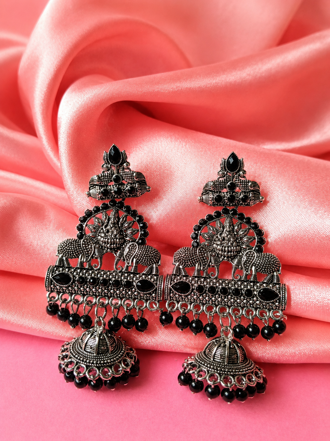 Ornate silver earrings with black beads on a pink fabric background