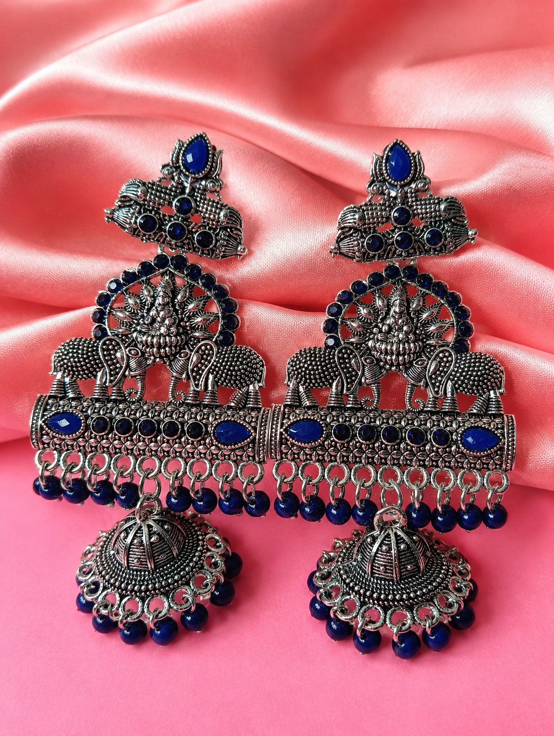 Ornate silver and blue earrings on a pink fabric background
