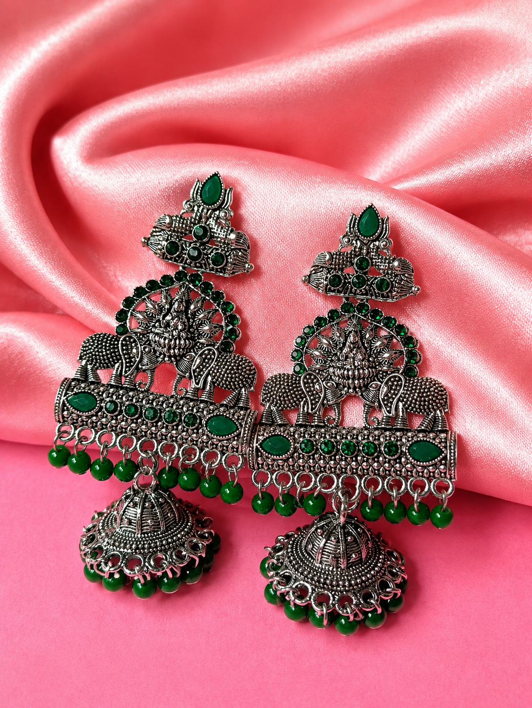 Ornate silver and green earrings on a pink satin background