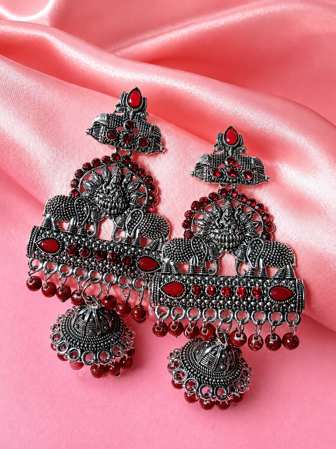 Ornate silver and red earrings on a pink satin background