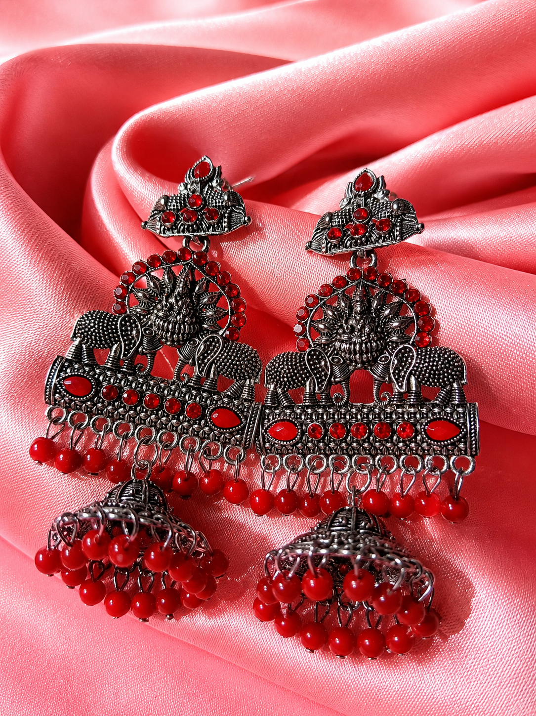 Ornate earrings with red beads on a pink fabric background