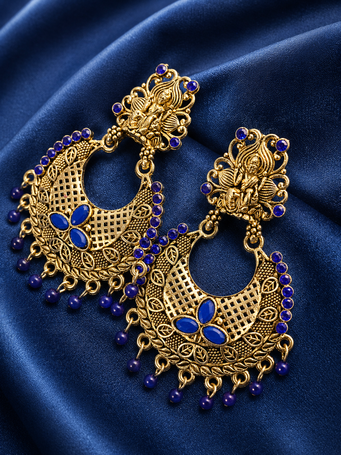 Ornate gold and blue earrings on a blue fabric background
