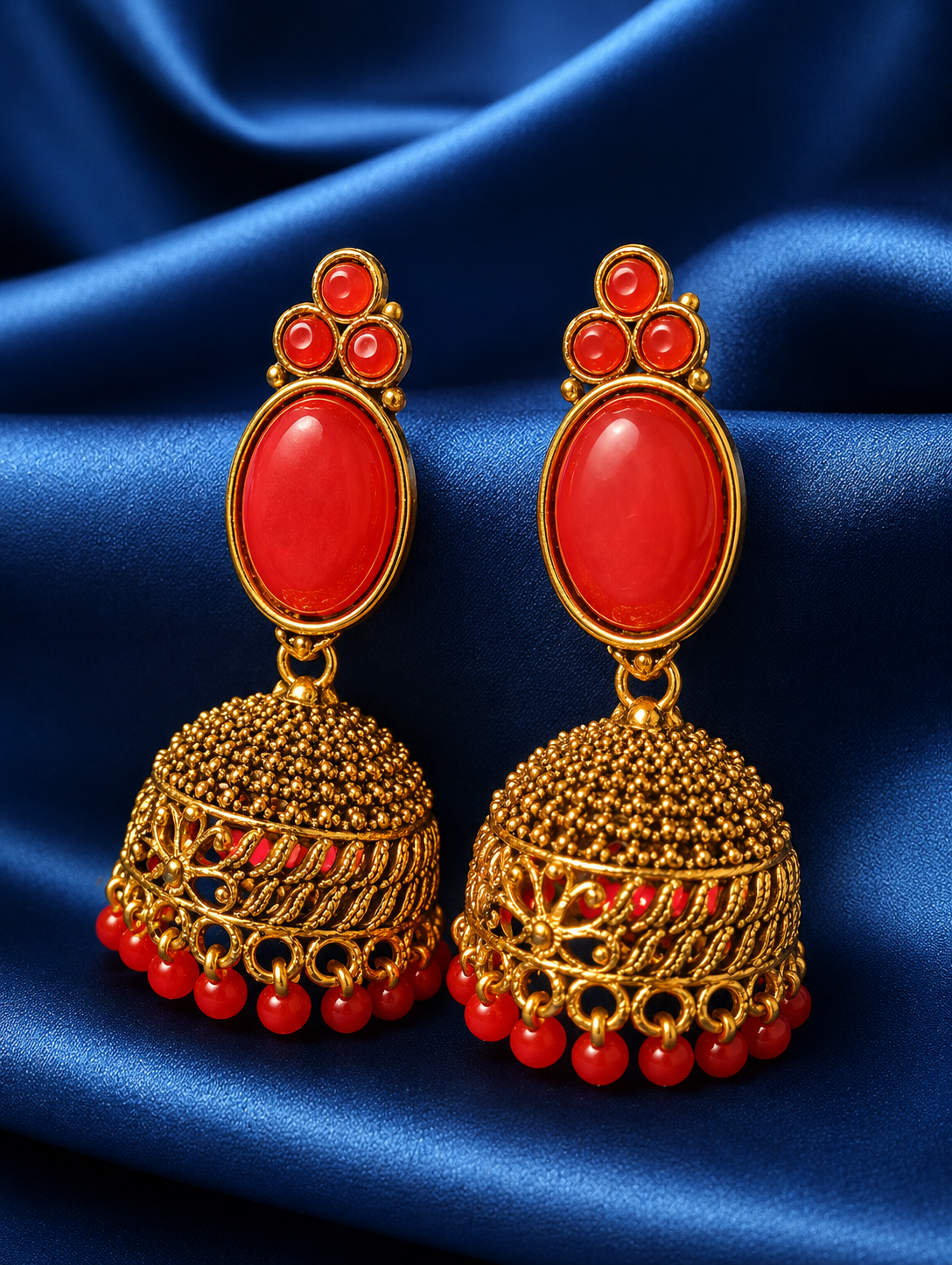 Gold earrings with red stones on a blue satin background