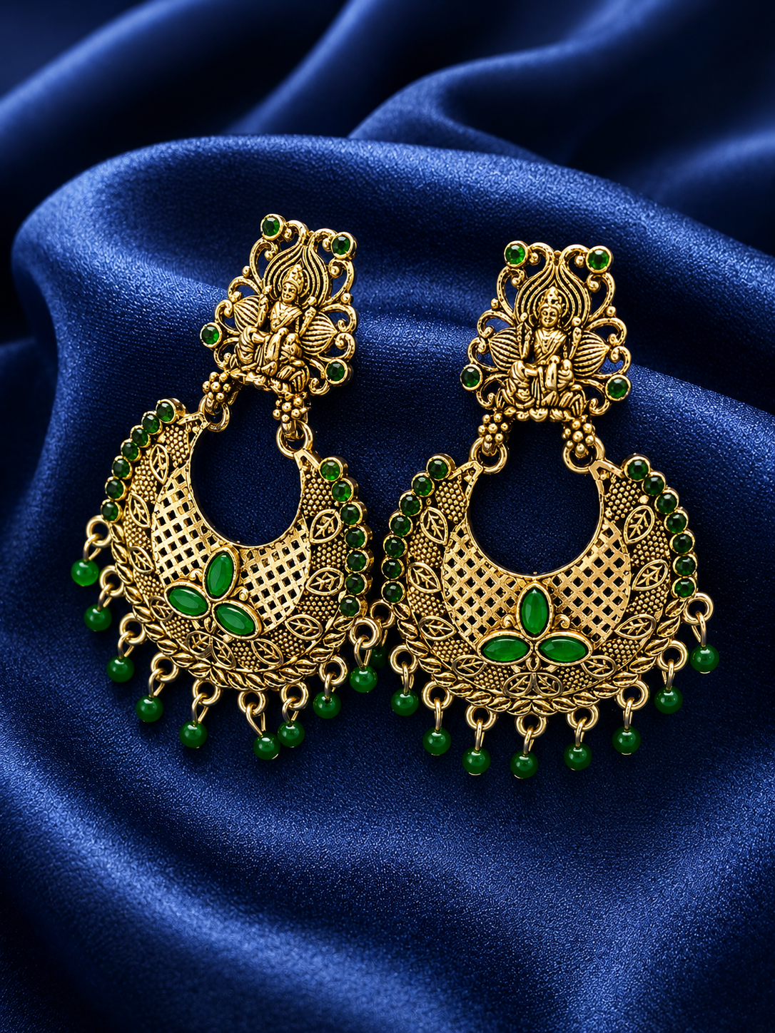 Gold and green earrings on a blue satin background