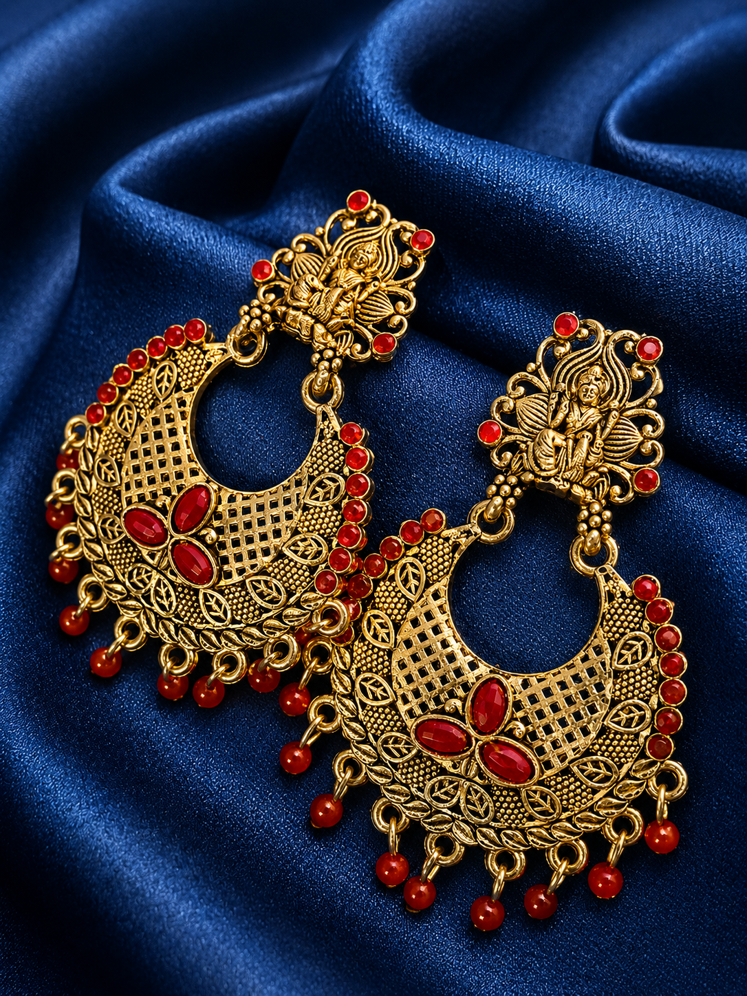 Ornate gold earrings with maroon stones on a blue fabric background