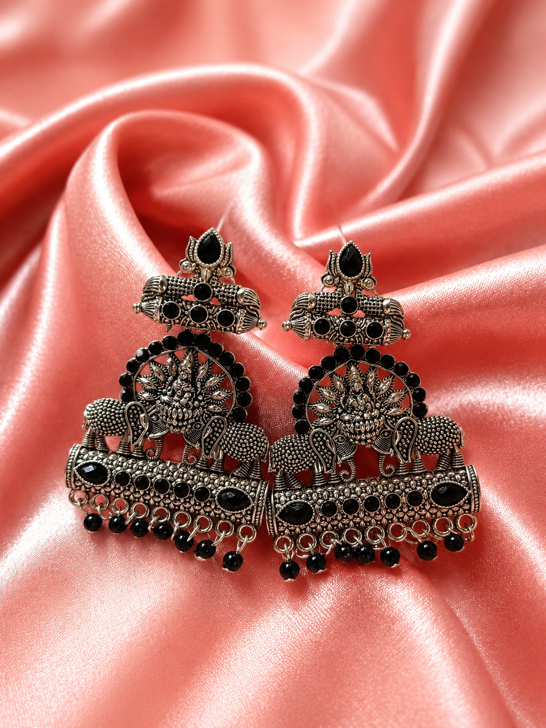 Ornate silver and black earrings on a pink fabric background
