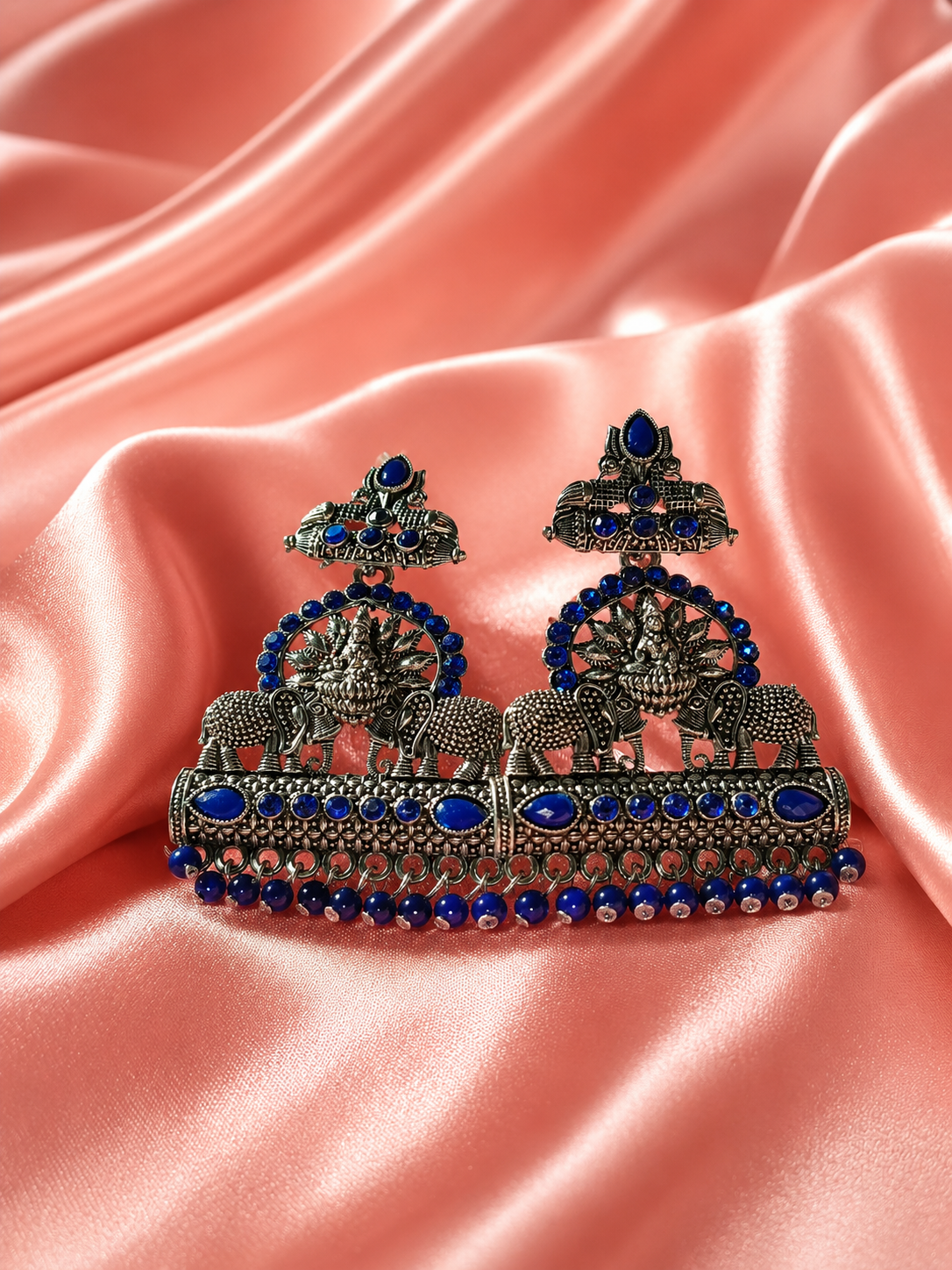 Ornate earrings with blue stones on a pink satin background