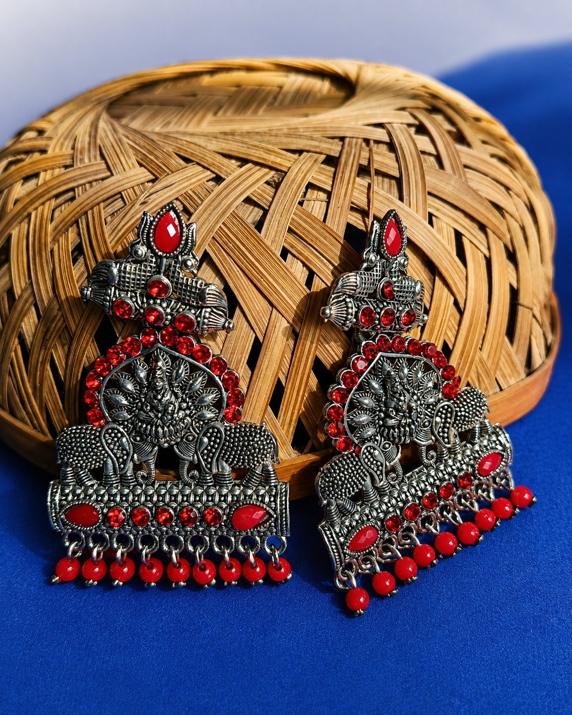 Ornate silver and Maroon earrings on a blue background with woven basket