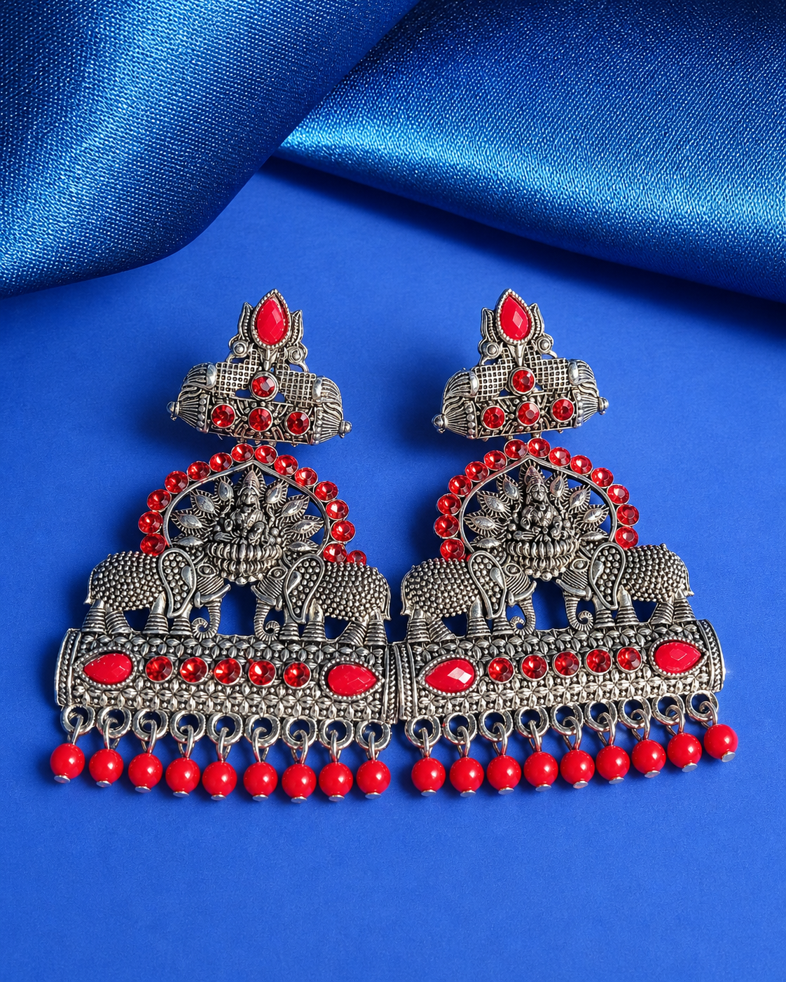 Ornate silver earrings with red stones on a blue fabric background