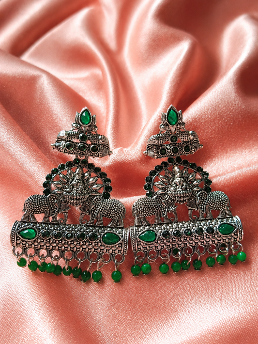 Ornate silver earrings with green gemstones on a pink satin background