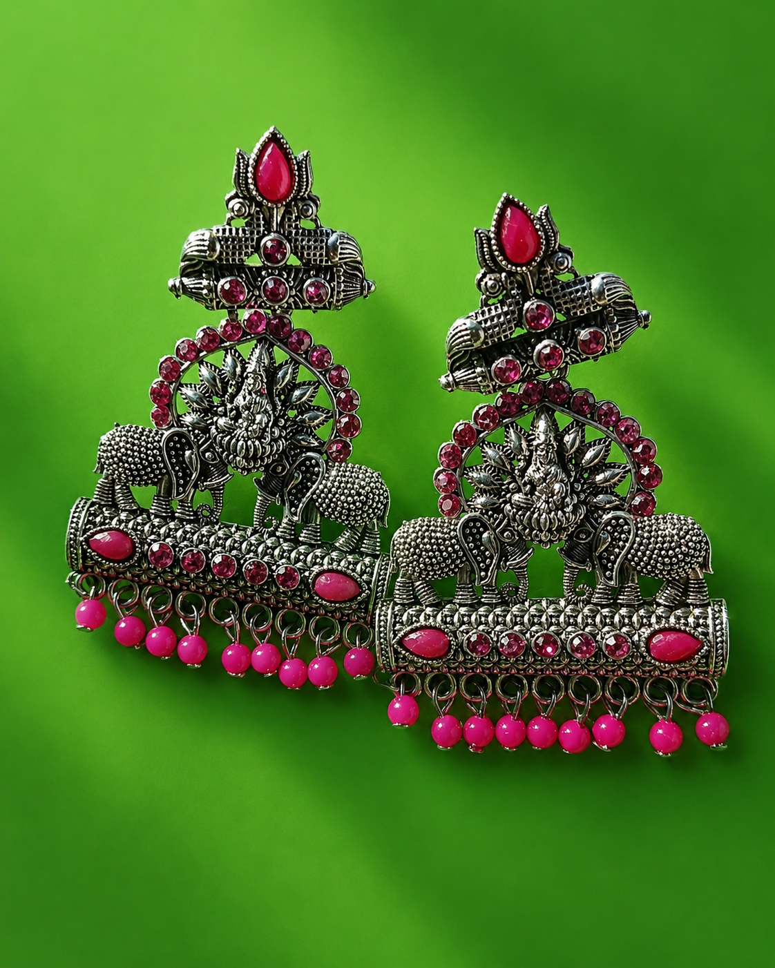 Ornate silver earrings with pink gemstones on a green background