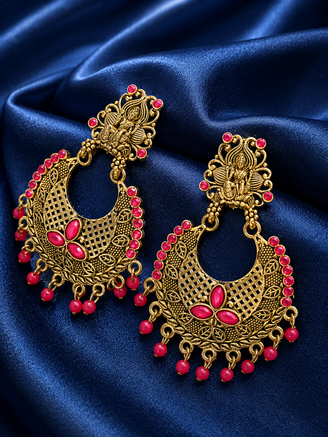 Ornate gold and pink earrings on a blue satin background