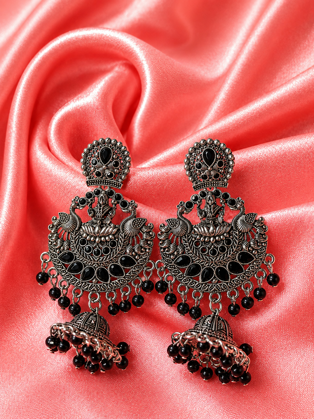 Ornate earrings with black beads on a pink satin background