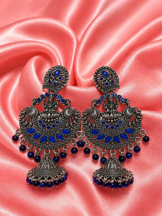 Ornate earrings with blue stones on a pink satin background