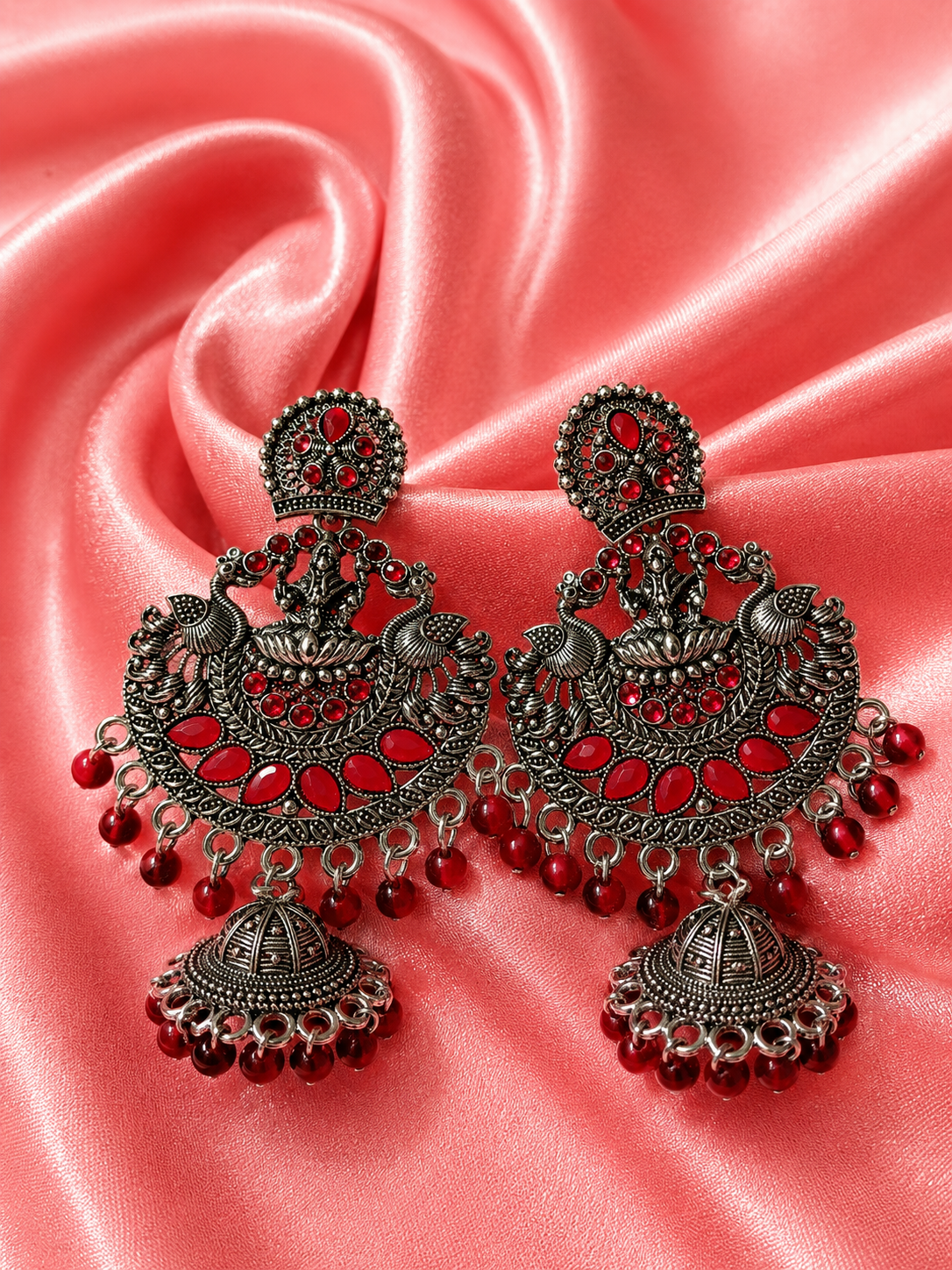 Ornate earrings with maroon
 stones on a pink satin background