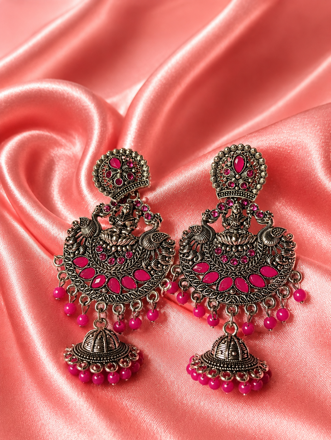 Ornate earrings with pink beads on a pink satin background