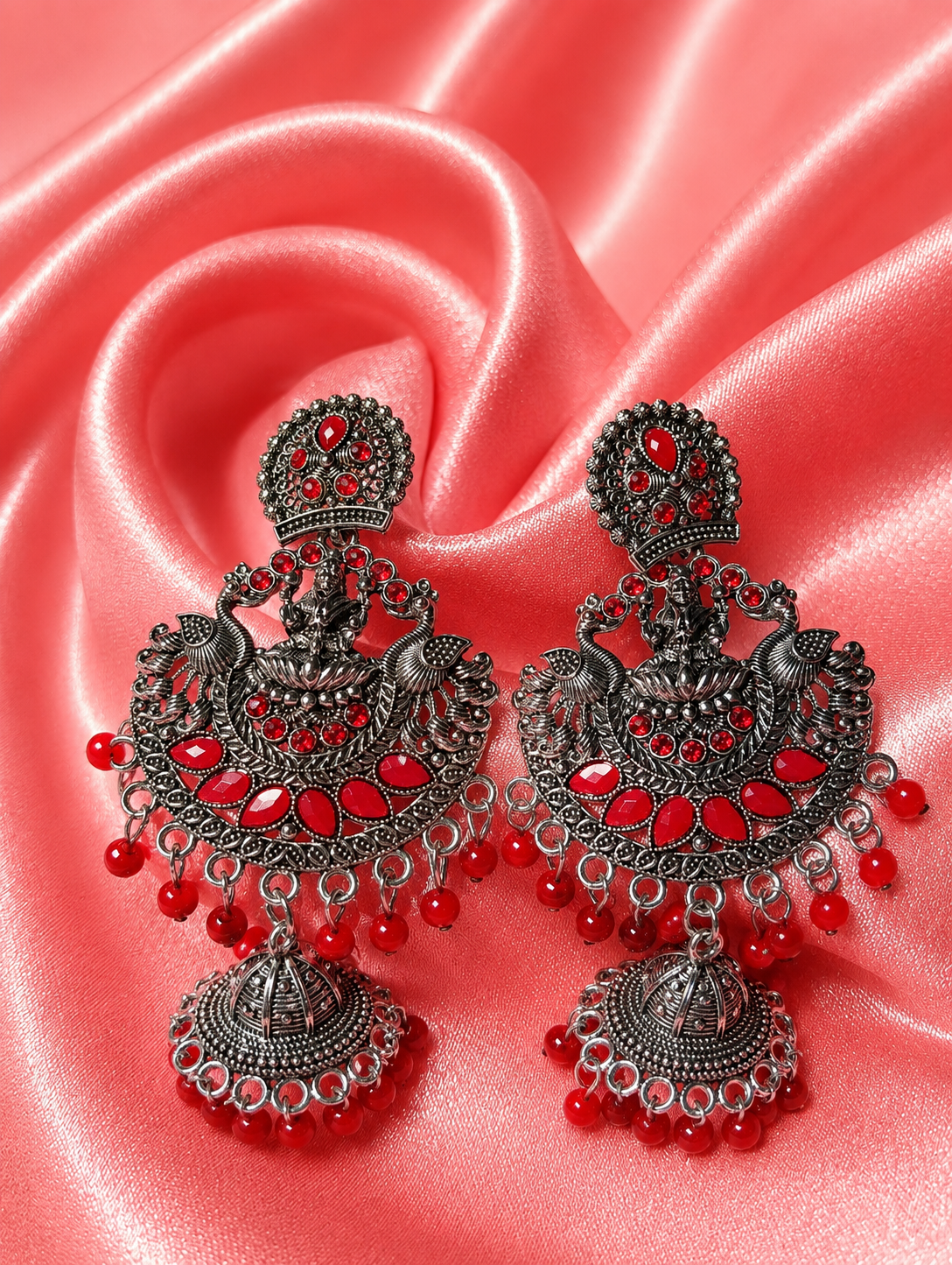 Ornate silver and red earrings on a pink satin background