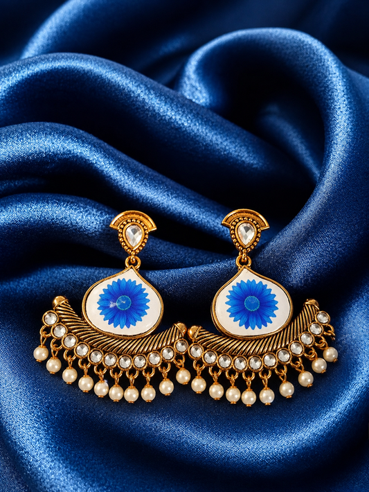 Ornate earrings with blue center and pearl details on a blue satin background