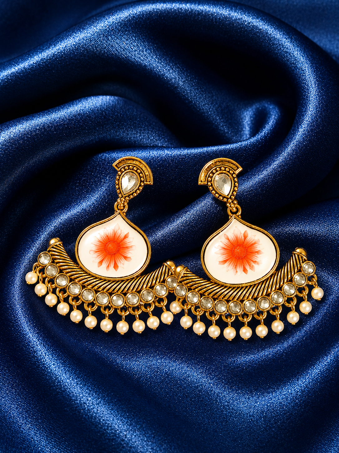 Ornate gold earrings with orange center and pearl-like stones on blue satin fabric