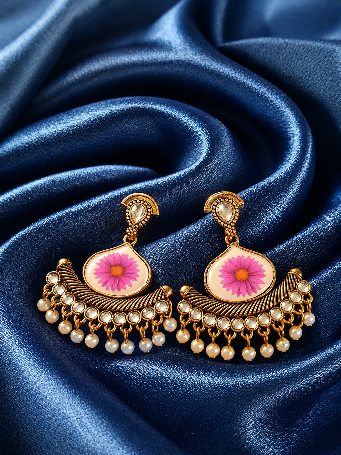 Ornate earrings with pink floral design on a blue satin background