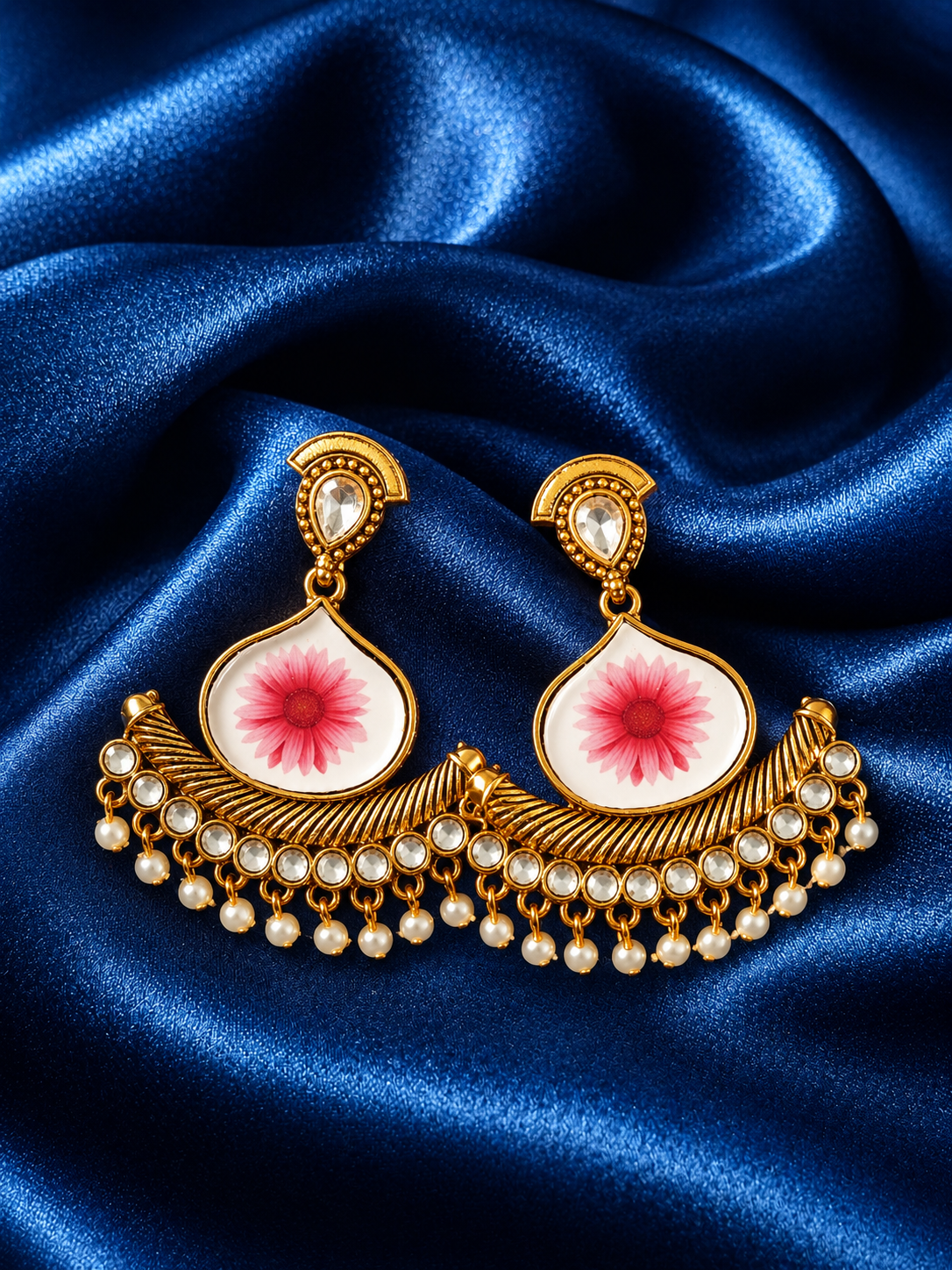 Ornate gold earrings with pink floral design on a blue satin background