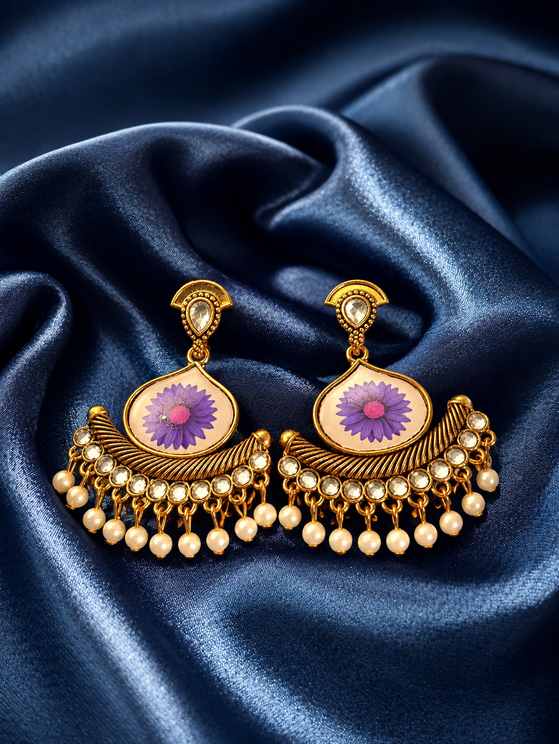 Gold earrings with purple gemstones on a blue satin background