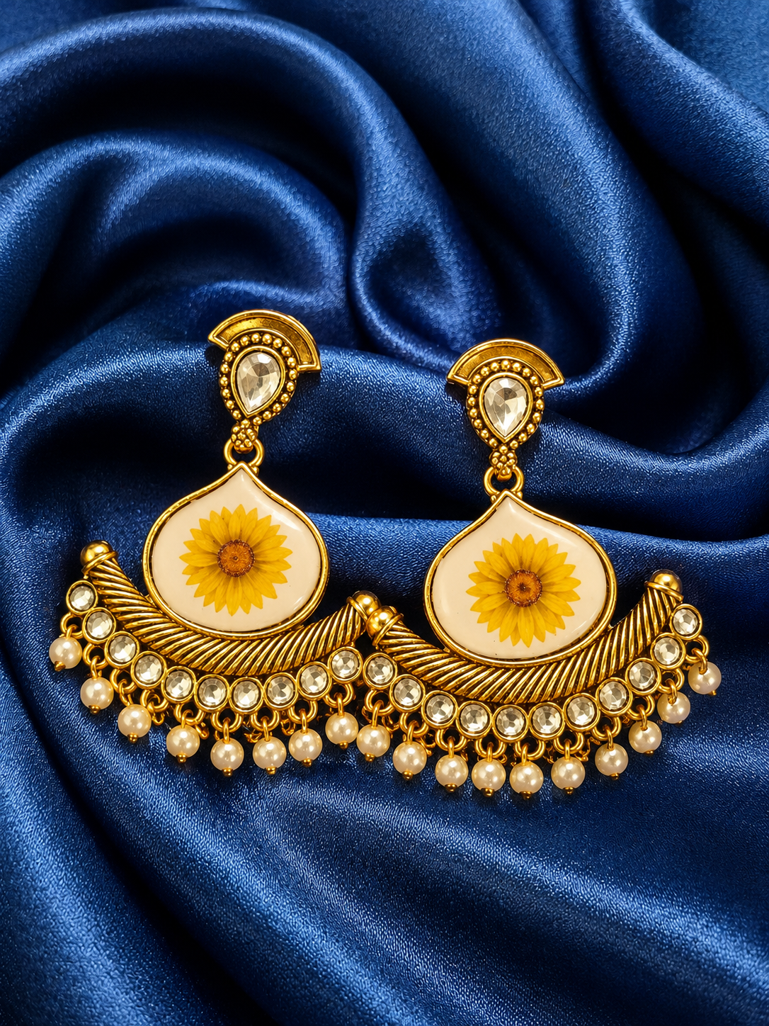 Gold earrings with sunflower design on a blue fabric background