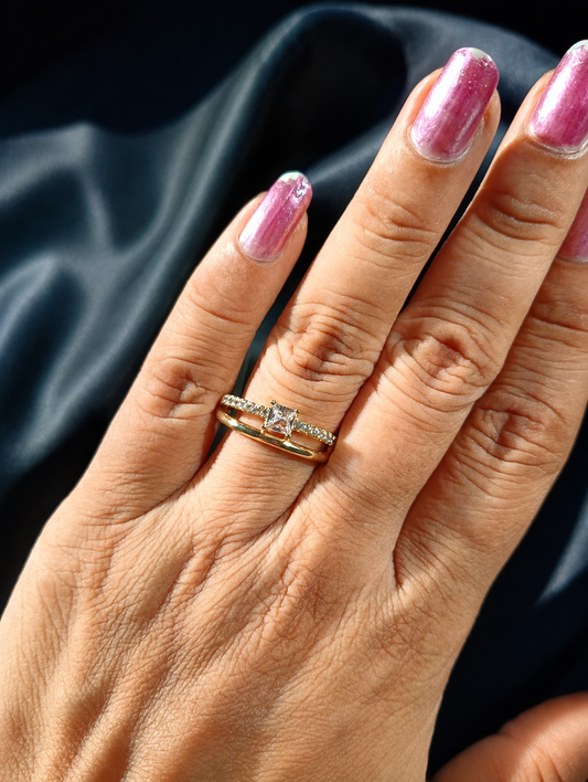 Hand with pink nail polish and a gold ring on a dark fabric background
